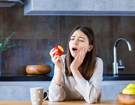 person eating an apple and holding their mouth in pain