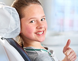 Young girl in dental chair giving thumbs up