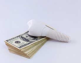 Model implant atop money representing the cost of dental implants in Cumming