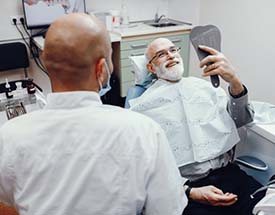 senior man looking at his new smile in the mirror after getting dental implants