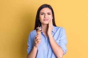 young woman with toothache holding ice cream cone against yellow background 