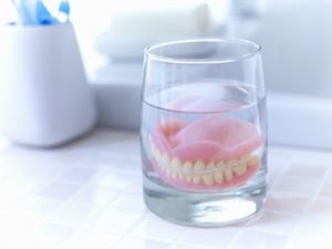 Dentures sitting in a glass of solution on a bathroom counter