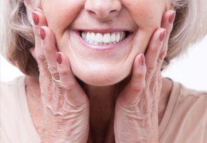 Lower half of woman's face smiling with dentures in holding her hands to her jaw